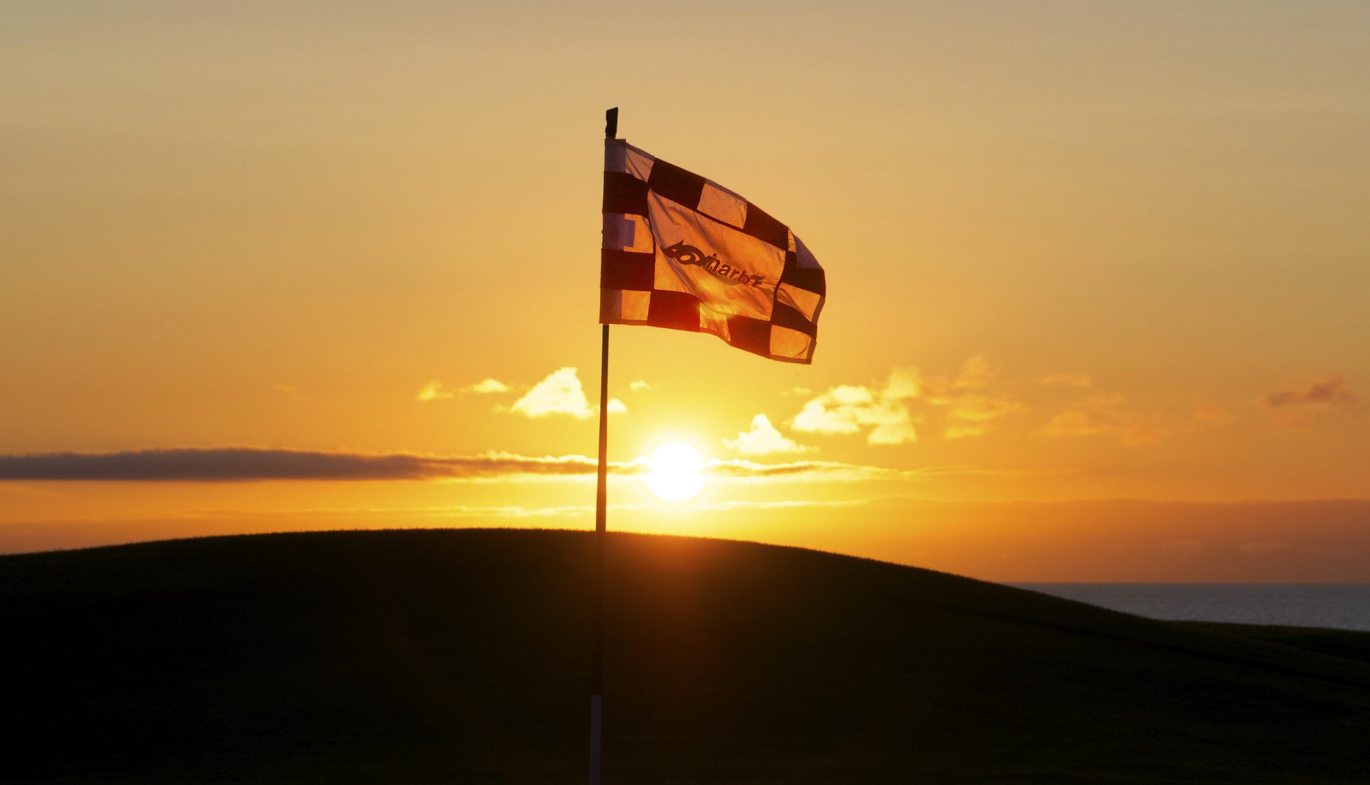 A golf flag silhouetted against a golden Fox Harb'r sunset